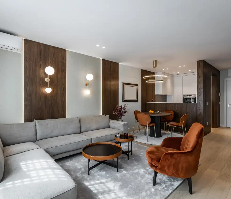 Living and dining room with dark wood wall panels, a grey sofa and an orange velvet armchair