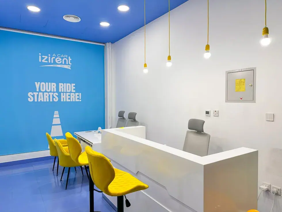 Car rental reception after fit-out: blue feature wall, white counter, yellow chairs and pendant lights