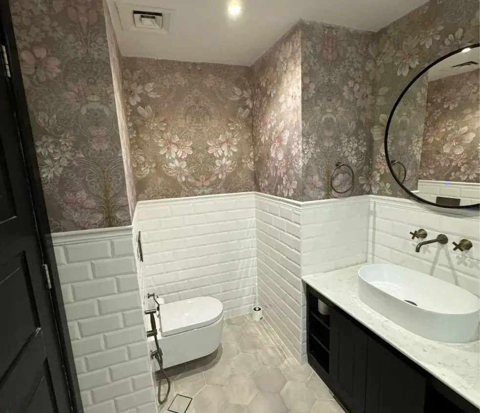 Renovated guest bathroom with white metro tiles, floral wallpaper and a round mirror