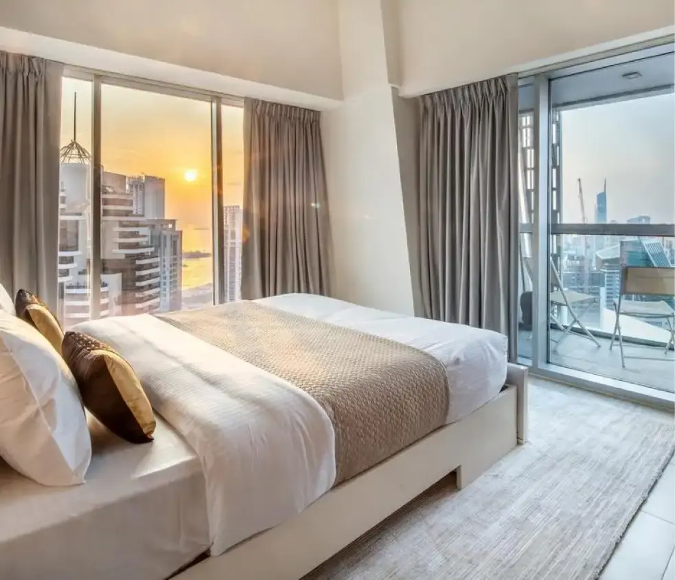 Bedroom with floor-to-ceiling windows and a balcony overlooking Dubai Marina at sunset